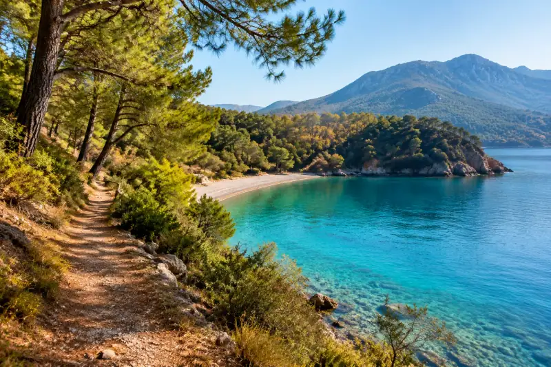 Adrasan Koyu’nda turkuaz deniz, sahil yürüyüş yolu ve çamlarla kaplı tepeler